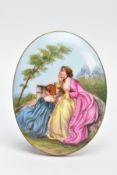 A LARGE PAINTED CERAMIC BROOCH, painted scene depicting two lady's in dresses sitting on a wall