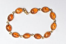 A 9CT GOLD AMBER LINE BRACELET, designed with a row of eleven oval amber cabochons, each collet