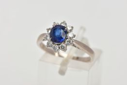 A SAPPHIRE AND DIAMOND CLUSTER RING, centring on a four claw set, oval cut blue sapphire, within a