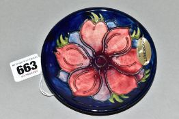 A MOORCROFT POTTERY CIRCULAR PIN DISH DECORATED WITH A RED/MAUVE ANEMONE ON A BLUE GROUND, with oval