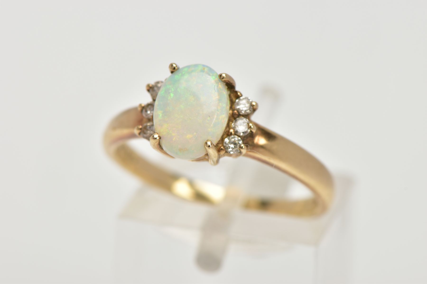 A 9CT GOLD OPAL AND DIAMOND RING, centring on a four claw set oval white opal cabochon, showing