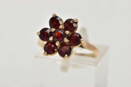 A YELLOW METAL GARNET CLUSTER RING, in the form of a flower cluster, set with seven circular cut