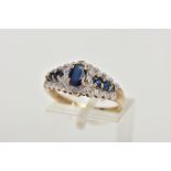 A 9CT GOLD SAPPHIRE RING, designed with a central four claw set, oval cut blue sapphire, flanked