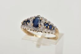 A 9CT GOLD SAPPHIRE RING, designed with a central four claw set, oval cut blue sapphire, flanked