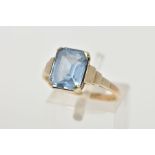 A YELLOW METAL RING, designed with an emerald cut pale blue stone assessed as synthetic spinel, step