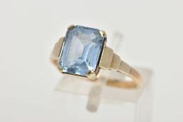 A YELLOW METAL RING, designed with an emerald cut pale blue stone assessed as synthetic spinel, step