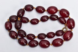 A CHERRY AMBER BAKELITE BEAD NECKLACE, a single row of graduated oval beads, largest measuring