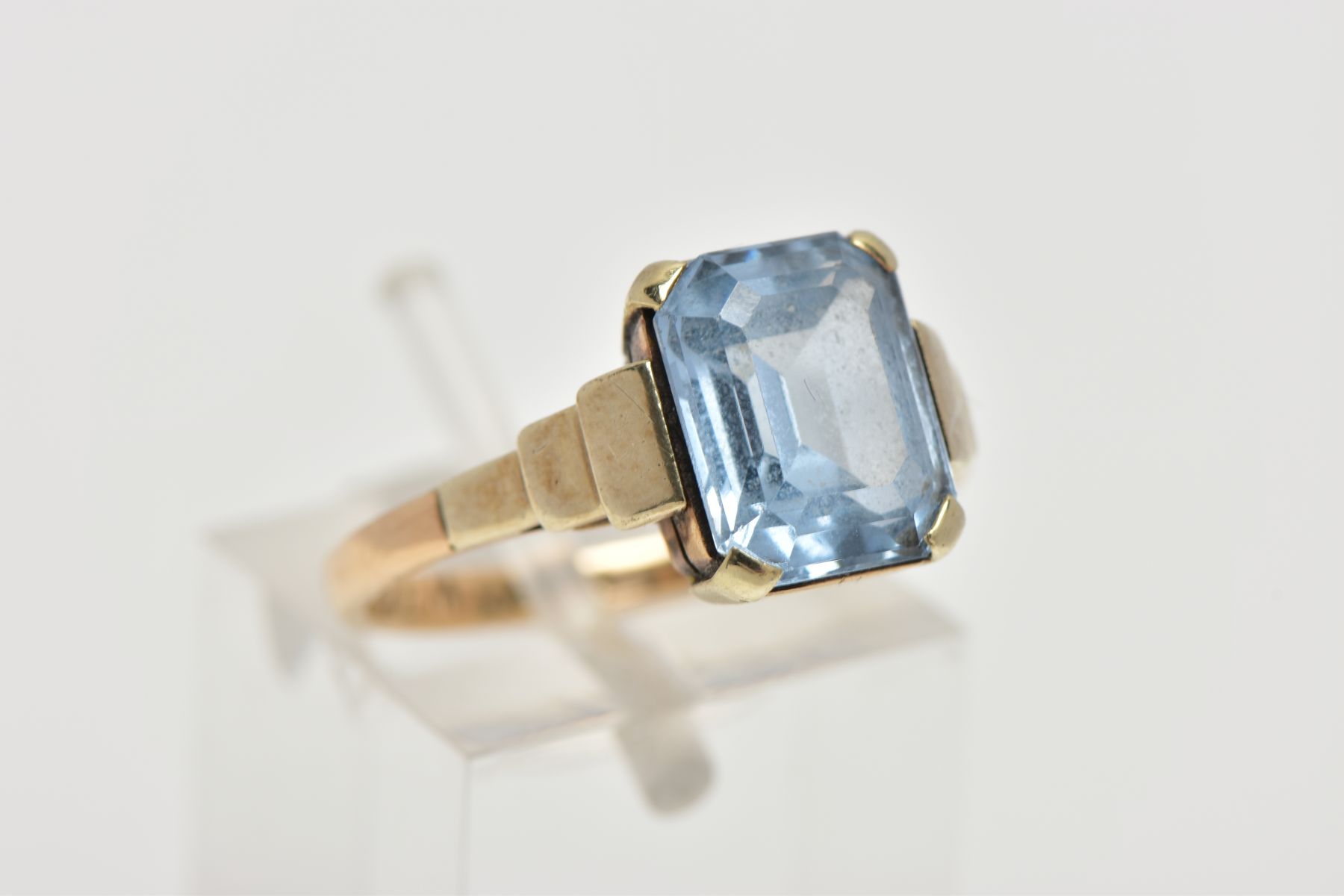 A YELLOW METAL RING, designed with an emerald cut pale blue stone assessed as synthetic spinel, step - Image 4 of 4