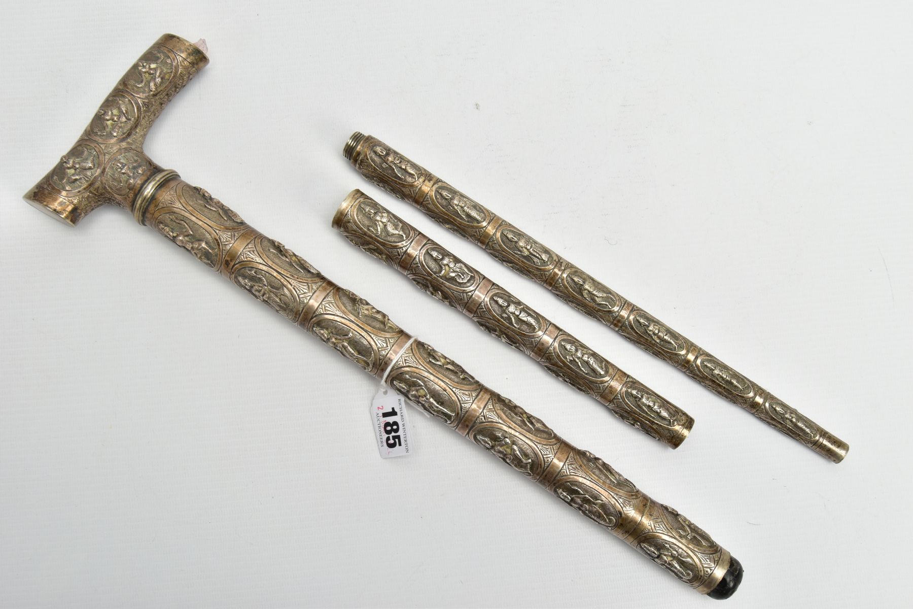 AN ASIAN WHITE METAL WALKING CANE, embossed religious figures throughout, can be taken apart into