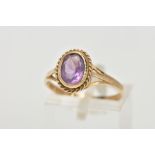 A 9CT GOLD AMETHYST RING, designed with an oval cut amethyst bezel set within a rope twist surround,