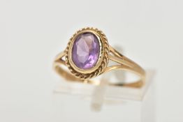 A 9CT GOLD AMETHYST RING, designed with an oval cut amethyst bezel set within a rope twist surround,