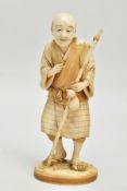 A JAPANESE MEIJI PERIOD IVORY OKIMONO, of a man standing holding a staff, on an oval base, the