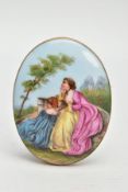 A LARGE PAINTED CERAMIC BROOCH, painted scene depicting two lady's in dresses sitting on a wall