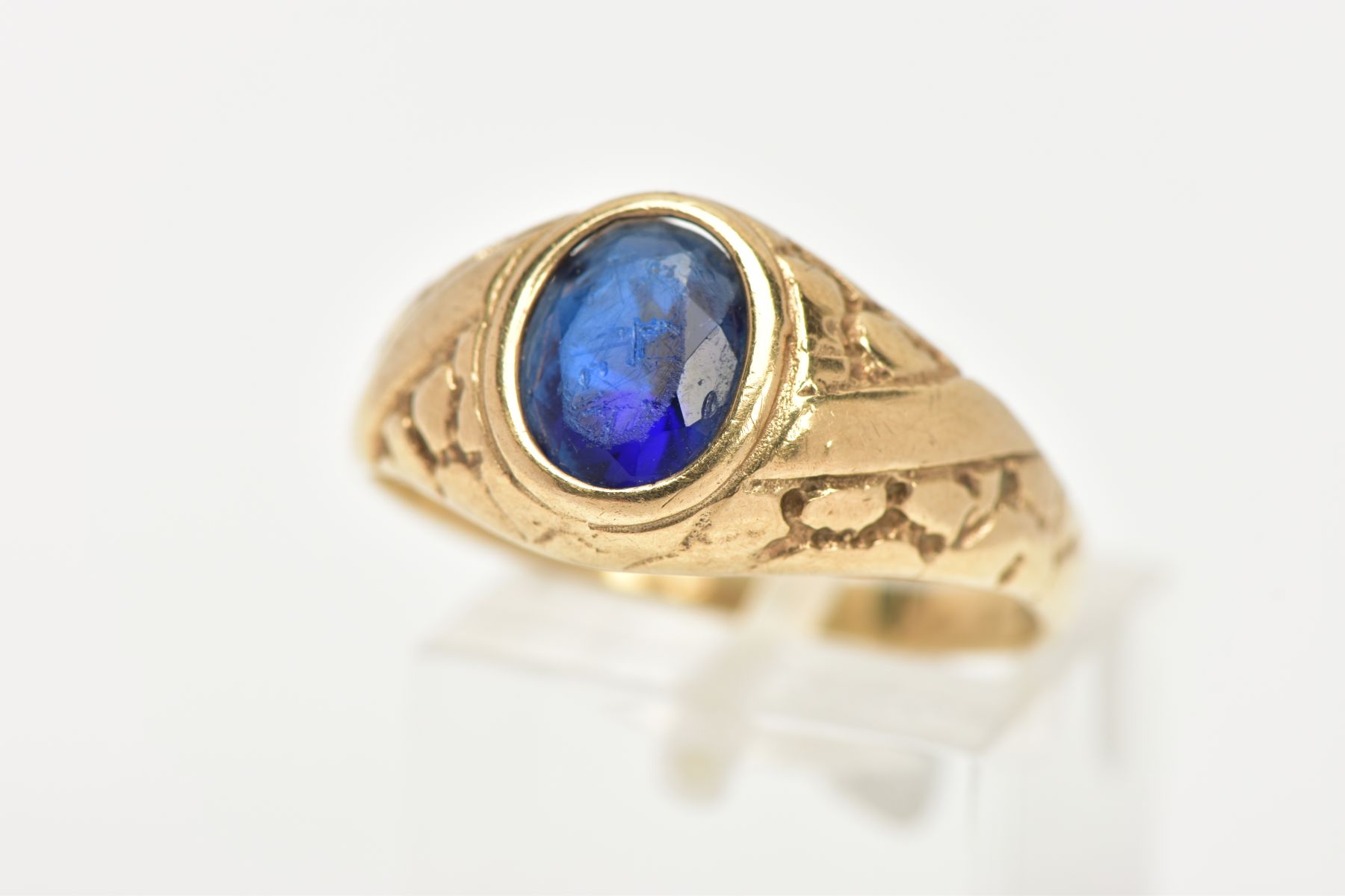 A 9CT GOLD SIGNET RING, set with an oval cut blue paste, bezel set, textured shoulders leading
