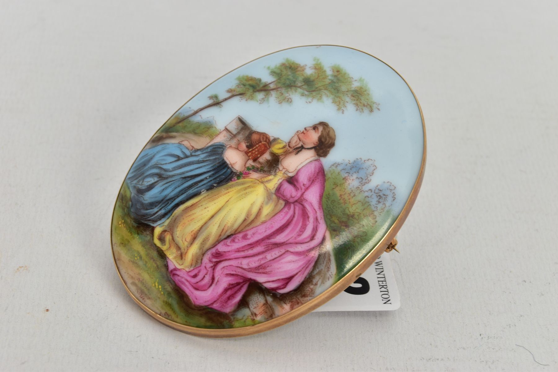 A LARGE PAINTED CERAMIC BROOCH, painted scene depicting two lady's in dresses sitting on a wall - Image 3 of 3