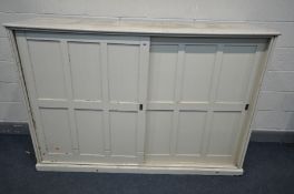 A LATE 19TH CENTURY LARGE CREAM PAINTED PINE SCHOOL CUPBOARD, with two panelled sliding doors,