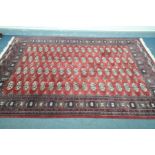 A LATE 20TH CENTURY RED WOOLEN TEKKIE GROUND RUG, with a multistrap border, length 270cm depth 189cm