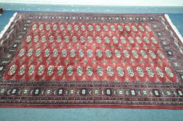 A LATE 20TH CENTURY RED WOOLEN TEKKIE GROUND RUG, with a multistrap border, length 270cm depth 189cm