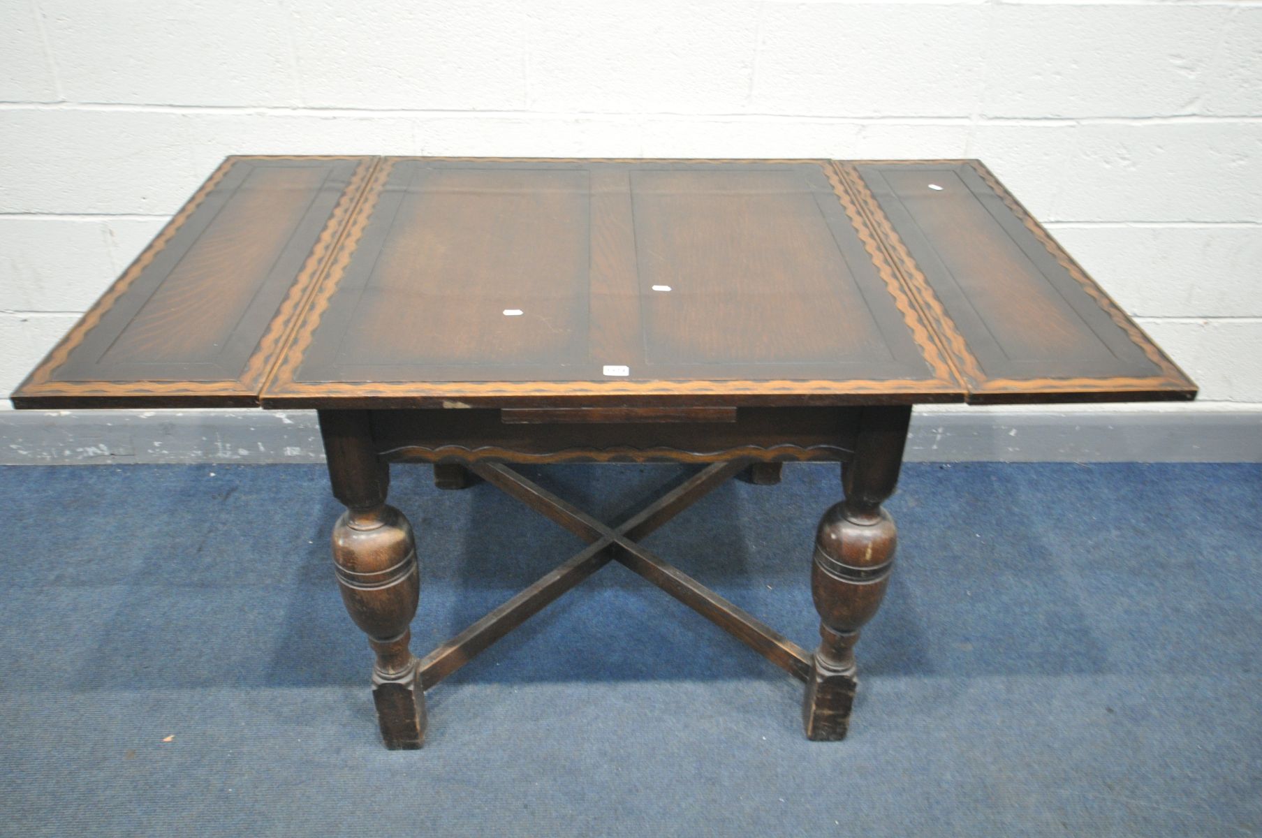 AN OAK DRAW LEAF DINING TABLE, with a wavy carved border, on bulbous legs, united by a cross