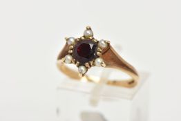 A 9CT GOLD GARNET AND SEED PEARL CLUSTER RING, centring on a circular cut garnet double claw set