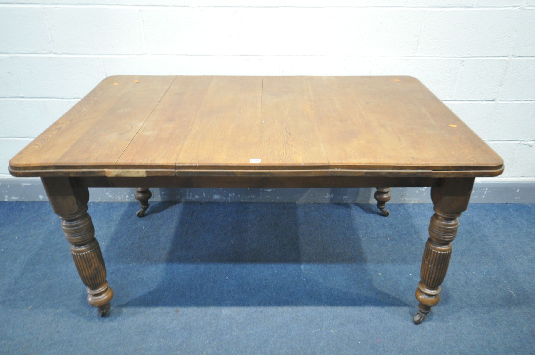 AN EDWARDIAN OAK DINING TABLE, on turned and fluted legs, on ceramic casters, width 153cm x depth