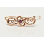 A VICTORIAN GOLD BROOCH, scrolled open work detailing with a central bezel set circular cut ruby,