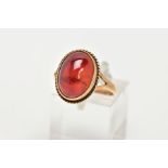 A 9CT GOLD RING, designed with a hollowed out, oval red cabochon, bezel set with a rope twist