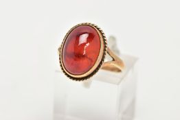 A 9CT GOLD RING, designed with a hollowed out, oval red cabochon, bezel set with a rope twist