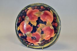 A MOORCROFT POTTERY SHALLOW BOWL DECORATED IN THE POMEGRANATE DESIGN ON A MOTTLED GREEN / BLUE