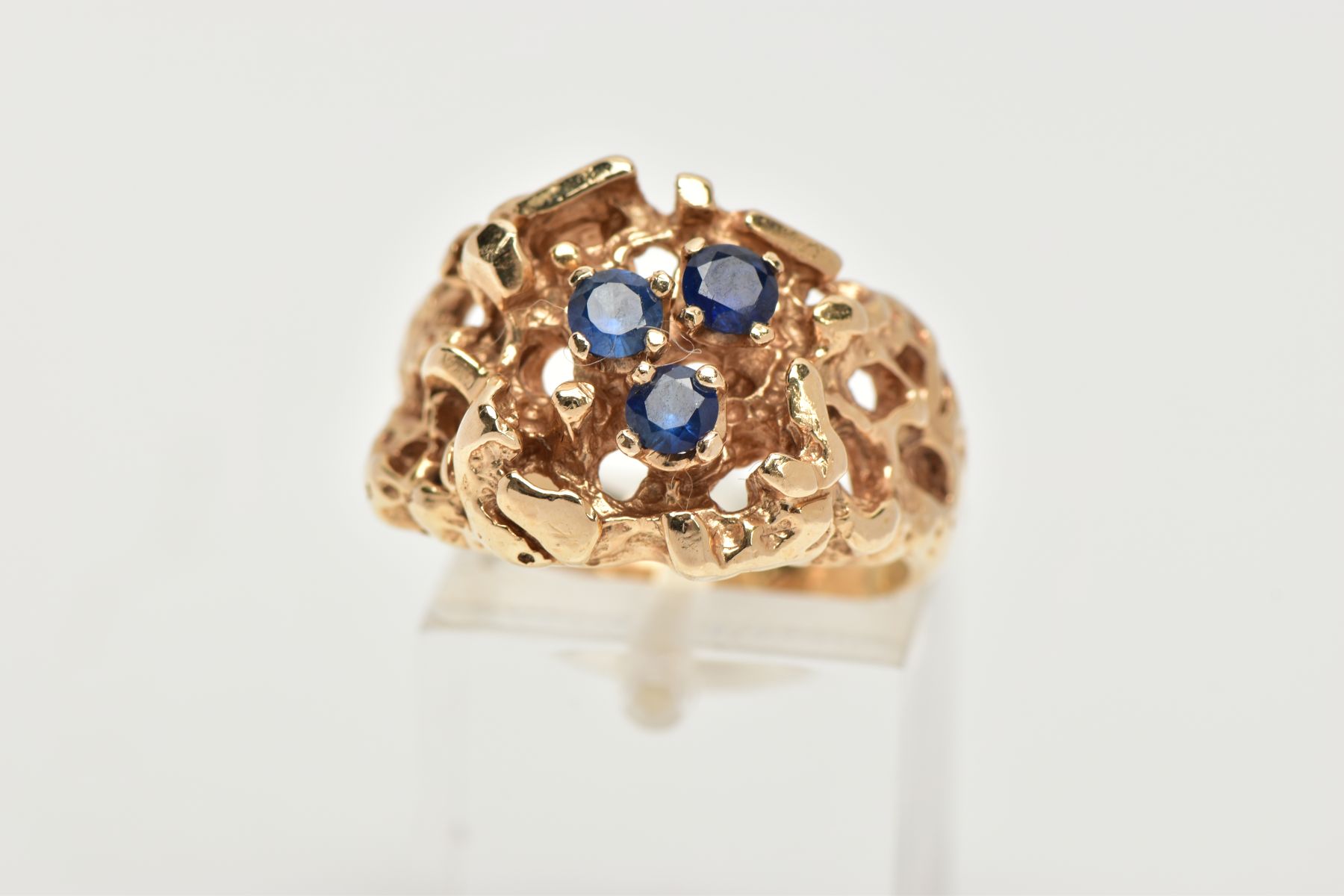 A YELLOW METAL ABSTRACT DRESS RING, an open work textured ring set with three circular cut blue