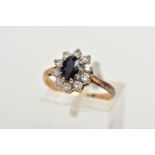 A YELLOW METAL SAPPHIRE AND DIAMOND CLUSTER RING, centring on an oval cut deep blue sapphire, within