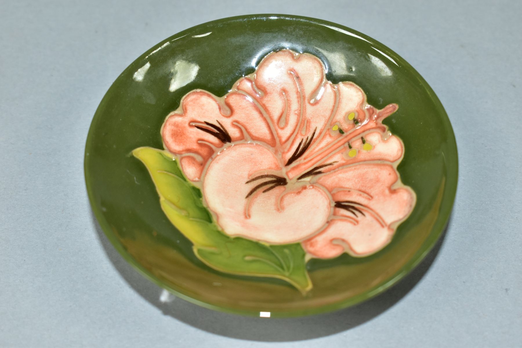 A MOORCROFT POTTERY CIRCULAR PIN DISH DECORATED WITH CORAL HIBISCUS ON A GREEN GROUND, faint - Image 3 of 4