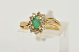 A YELLOW METAL EMERALD AND DIAMOND RING, an oval cut emerald prong set within a surround of twelve