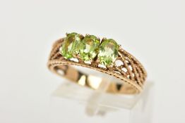 A 9CT GOLD PERIDOT RING, three oval cut peridots prong set in yellow gold, leading on to an open