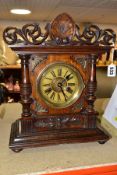 A LATE 19TH CENTURY WALNUT AND STAINED MANTEL CLOCK, foliate carved pediment, printed dial with