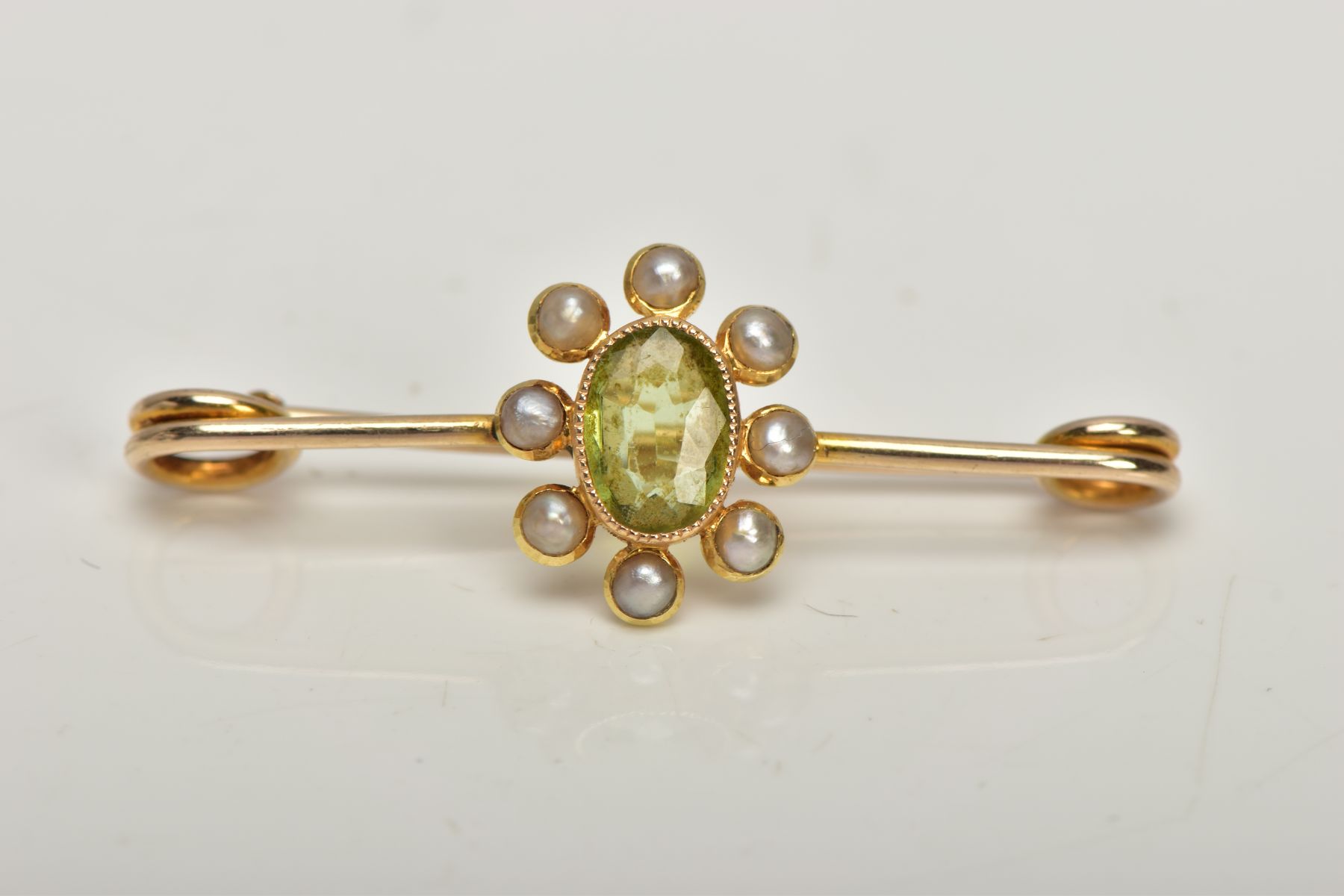 A YELLOW METAL PERIDOT AND SPLIT PEARL BAR BROOCH, the oval collet set peridot, within a split pearl