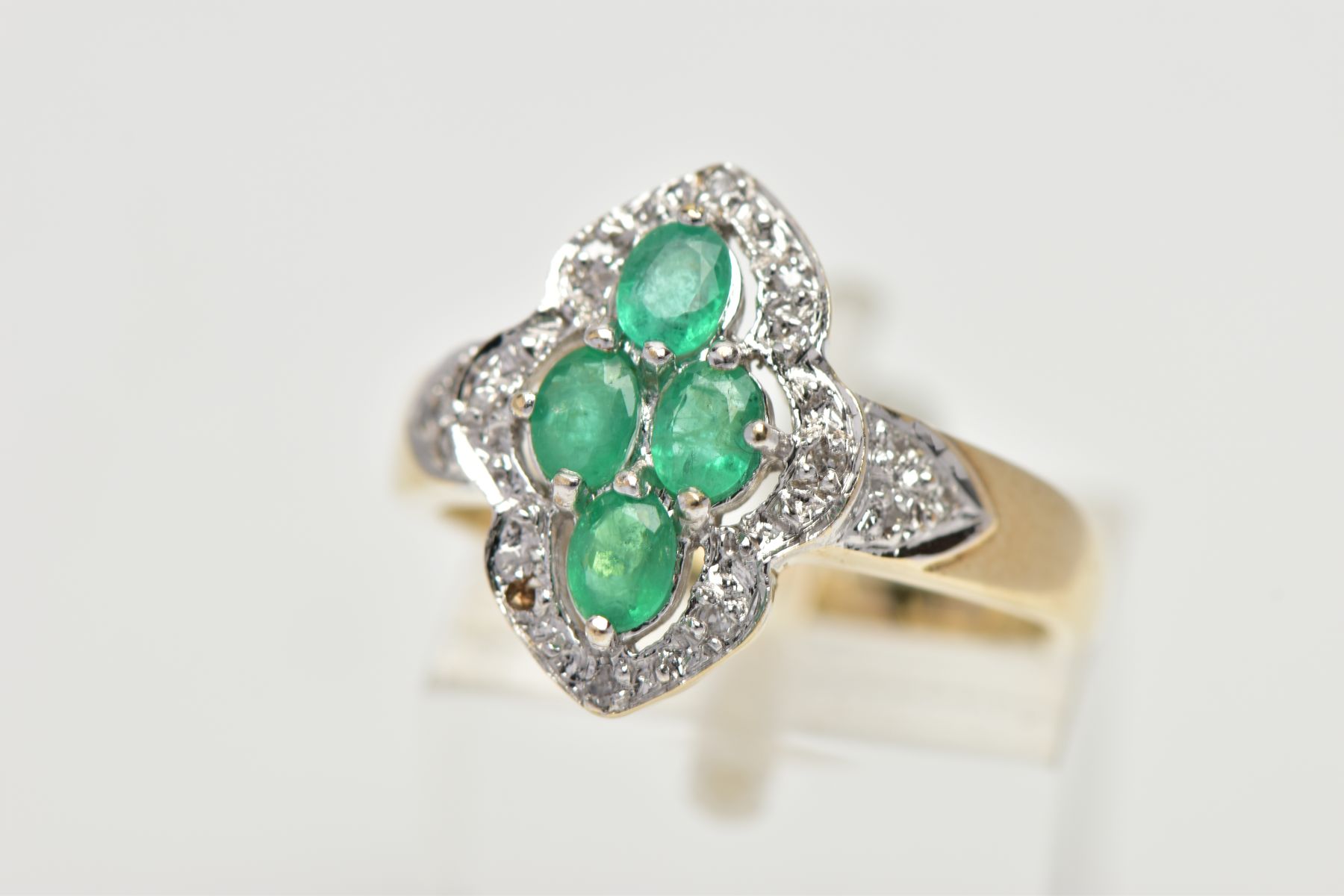A 9CT YELLOW AND WHITE GOLD EMERALD AND DIAMOND DRESS RING, set with four oval cut emeralds,