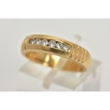 A YELLOW METAL DIAMOND RING, wide band measuring approximately 4.7mm, designed with a row of channel