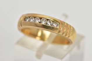 A YELLOW METAL DIAMOND RING, wide band measuring approximately 4.7mm, designed with a row of channel