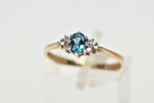 A 9CT YELLOW GOLD TOPAZ AND DIAMOND DRESS RING, set with a principal oval cut blue topaz, flanked to