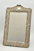 AN EDWARDIAN SILVER MOUNTED EASEL BACK MIRROR, embossed with a ribbon over a vacant cartouche,