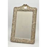 AN EDWARDIAN SILVER MOUNTED EASEL BACK MIRROR, embossed with a ribbon over a vacant cartouche,