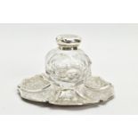 A VICTORIAN SILVER AND GLASS INKWELL ON STAND, of wavy circular outline, foliate engraved decoration