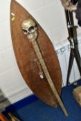 A WOODEN SHIELD AND STAFF, the staff has a carved skull on top, length 110cm, the shield is carved