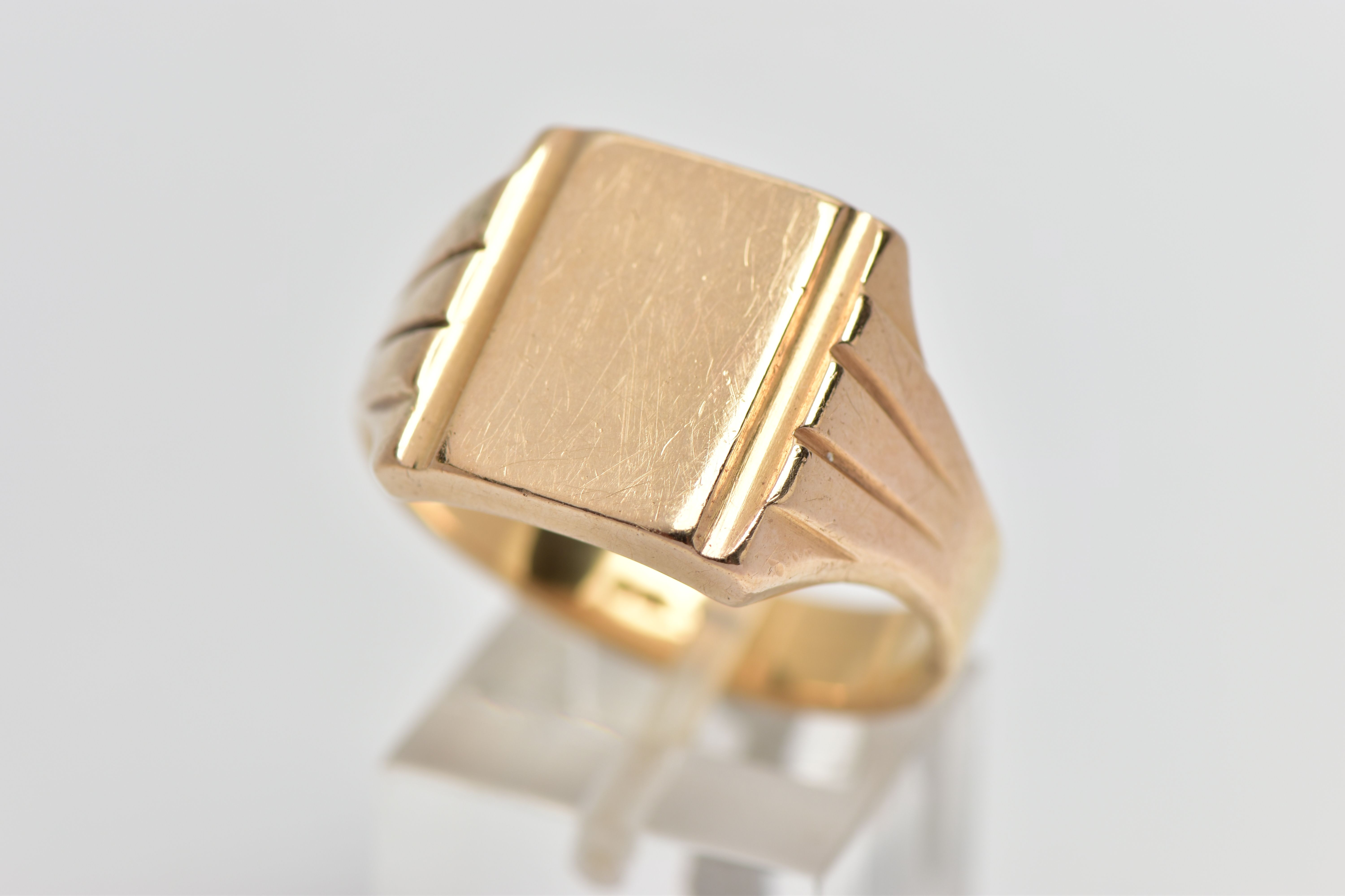 A GENTLEMANS YELLOW METAL SIGNET RING, designed as a rectangular shape plain polished panel, with