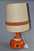 A 1960S ORANGE GLAZED TABLE LAMP BEARING HERDA LABEL, fitted with a conical hessian and woollen