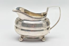 A SILVER MILK JUG, with floral engraved detail, atop an oval pedestal and spherical feet, with plain