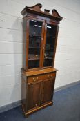 A SLIM EDWARDIAN WALNUT GLAZED TWO DOOR BOOKCASE, with one long drawer and double fielded panel