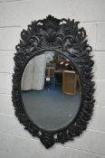 AN EARLY 20TH CENTURY EBONISED WALL MIRROR, with open foliate decoration, and beveled mirror