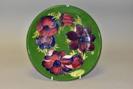 A MOORCROFT POTTERY CHARGER DECORATED WITH PURPLE PINK ANEMONES ON A GREEN GROUND, a second,